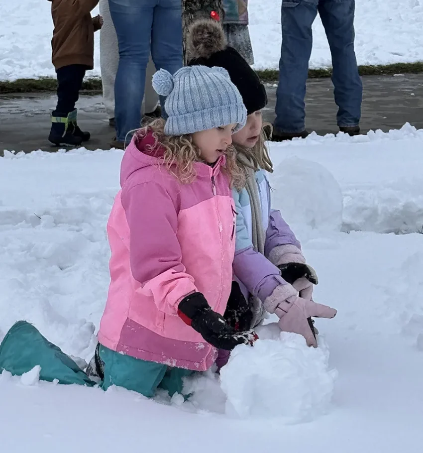 Two young girls roll a ball of snow to start a new snowman.