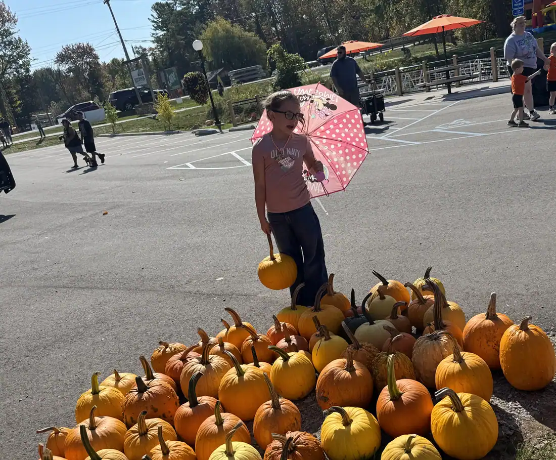 kid with umbrella and selecting a pumpkin from several.
